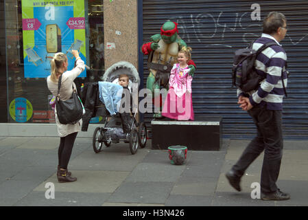 Glasgow Straße Szenen Familie Selbstporträt mit Kostüm Straße Straßenmusiker Ninja Schildkröte Kind als Prinzessin Stockfoto