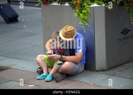 Glasgow Straße Szenen Vater und Sohn nutzen Handy zusammen sitzend auf Boden Stockfoto