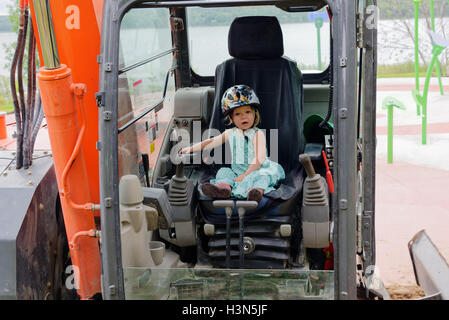 Ein junges Mädchen (2 Jahre alt) sitzt eine JCB (Bagger) Kabine vorgibt, es zu betreiben. Stockfoto