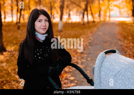 Junge glückliche Mutter mit Kinderwagen im Herbst park Stockfoto