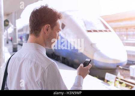 Junge Männchen mit app auf dem Smartphone während Geschäftsreisen mit dem Zug im Hintergrund Stockfoto