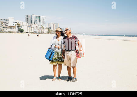 Älteres Paar zu Fuß am Strand, Tragetaschen für Picknick, Long Beach, Kalifornien, USA Stockfoto