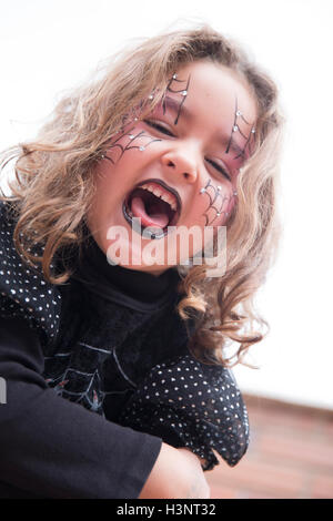 Gruselige kleine Mädchen in schwarz Halloween-Kostüm und lackierten Webs auf Gesicht mit offenem Mund. Stockfoto