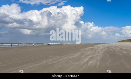 Menschen, die genießen einen Spaziergang an einem Sandstrand an der Nordsee unter hoch aufragenden weißen Cumulus Wolke Formationen am blauen Himmel Stockfoto