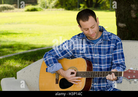 Mann, spielt akustischen Gitarre auf einer Parkbank, Musik zu schaffen. Stockfoto