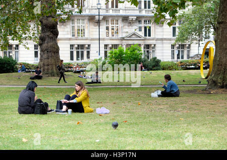 Junge Frauen sitzen im Cavendish Square Gardens in der Nähe von Harley Street im Herbst West-London, England Uk KATHY DEWITT Stockfoto