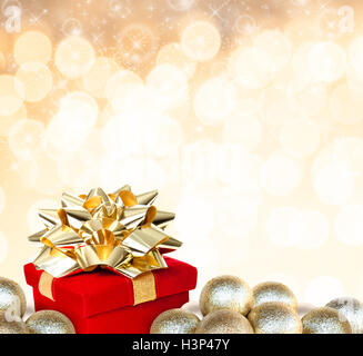 Rot Weihnachtsgeschenk mit Goldband umgeben Christbaumkugel Ornamente defokussierten Hintergrund golden leuchtet und funkelt. Stockfoto
