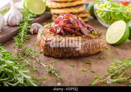 Leckeres Rindersteak mit Pfeffer, Knoblauch und karamellisierten Zwiebeln, Kartoffelpuffer hinter Stockfoto