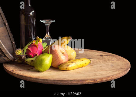 Obst und ein Glas Wein auf einem Holztablett mit einem schwarzen Hintergrund. Stockfoto