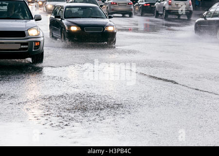 Autos fahren auf der Straße mit Wasserpfützen bei starkem Regen mit Wasser spritzt von den Rädern Stockfoto