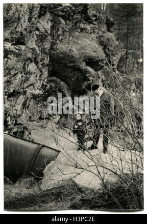 Deutschland - ca. 1970er Jahre: Mann mittleren Alters in einem Schaffell Mantel zu Fuß mit seinem Enkel in den Ausläufern Stockfoto