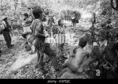 CHALATENANGO, EL SALVADOR, FEB 1984: - innerhalb der FPL Zonen Control A Guerillagruppe FPL-Männer und Frauen Kämpfer Rest und nehmen Wasser aus einem Stream. Stockfoto