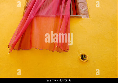 Roter Netzfenstervorhang auf gelb bemalter Wand in bosa, sardinien, italien Stockfoto