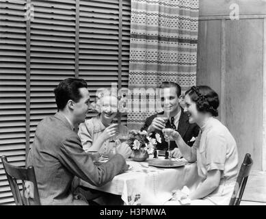 1930S 1940S ZWEI PAARE MANN FRAU AM ESSTISCH MIT COCKTAILS TOASTEN RESTAURANT JALOUSIEN VORHÄNGE Stockfoto