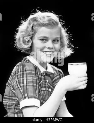 1930S 1940S LÄCHELND BLOND GIRL KAROHEMD HOLDING GLAS MILCH BLICK IN DIE KAMERA Stockfoto