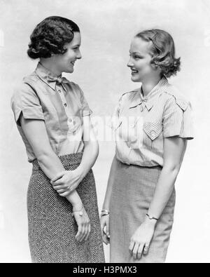 1930ER JAHREN ZWEI FRAUEN REDEN LÄCHELND MIT ANGENEHMEN GESPRÄCH Stockfoto