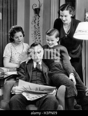 1940ER JAHRE FAMILIE VON VIER FRAU MUTTER TOCHTER MÄDCHEN UND SOHN TEENAGER SITZEN VATER MANN LESEN ZEITUNG Stockfoto