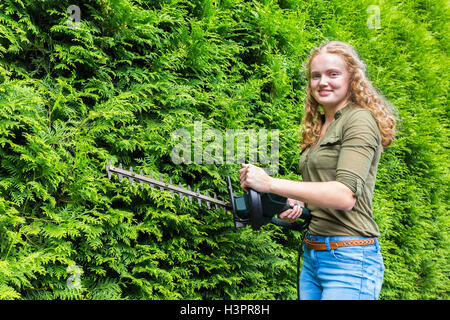 Kaukasische Mädchen halten Heckenschere auf grüne Nadelbäume Stockfoto