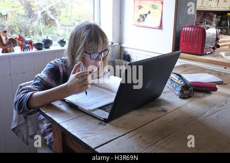 Ein 13 Jahre altes Mädchen, die ihre Hausaufgaben auf dem Küchentisch mit ihre Pyjamas auf. Stockfoto