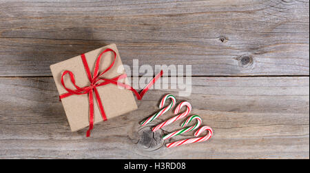 Draufsicht auf ein verpacktes Geschenk mit Zuckerstangen auf rustikalen Holz. Stockfoto