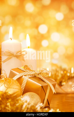 Goldene Christbaumkugeln, Kerzen und ein Geschenk auf einer hell glitzernden gold Hintergrund. Stockfoto