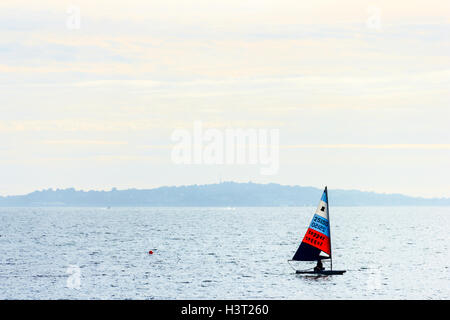 Eine Person Segeln eine kleine Jolle oder Yacht in den Abend in Weymouth Bay, Dorset, Großbritannien Stockfoto