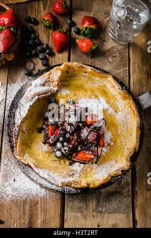 Holländische Baby-Pfannkuchen mit Beeren und Schokolade, gebacken im Ofen auf Eisenpfanne, besten Pfannkuchen immer!!! Stockfoto