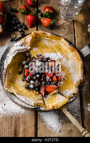 Holländische Baby-Pfannkuchen mit Beeren und Schokolade, gebacken im Ofen auf Eisenpfanne, besten Pfannkuchen immer!!! Stockfoto