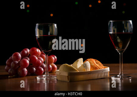 Komposition mit Wein, Käse, Nüssen und Trauben auf Holztisch, auf schwarzem Hintergrund Stockfoto