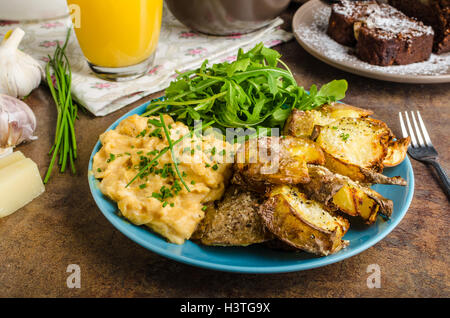 Knusprige zerschlagen Kartoffeln, Rührei und kleinen Salat, Saft und Kuchen zum Frühstück Stockfoto