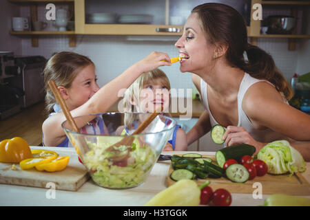 Kinder füttern ein Stück gelbe Paprika, Mutter in der Küche Stockfoto