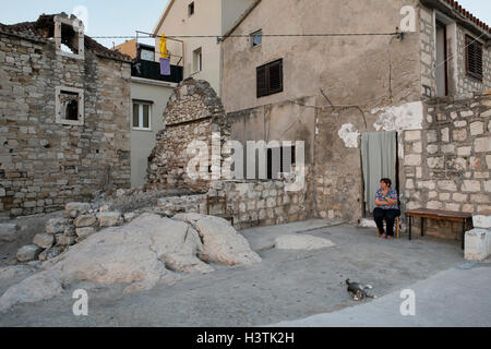 Eine ältere Frau sitzt vor ihrem Haus an der adriatischen Küste. Kastela, Split-Dalmatien, Kroatien, Europa. Stockfoto