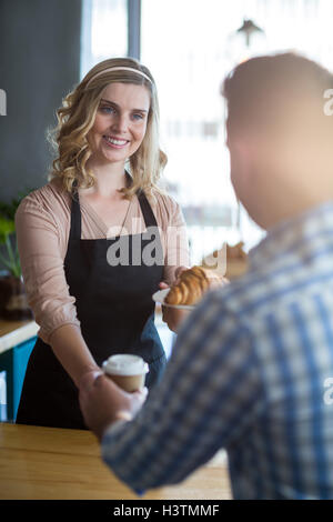 Kellnerin serviert eine Tasse Kaffee und ein Croissant an Kunden Stockfoto