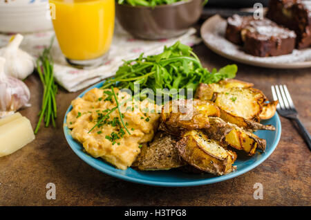 Knusprige zerschlagen Kartoffeln, Rührei und kleinen Salat, Saft und Kuchen zum Frühstück Stockfoto