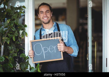 Porträt von lächelnden Kellner zeigt Tafel mit Schild "geöffnet" Stockfoto