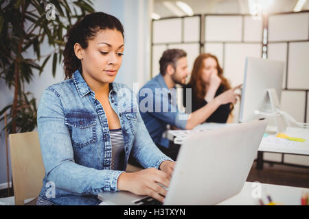 Kreative Geschäftsfrau mit Laptop an der Rezeption gegen Mitarbeiter Stockfoto