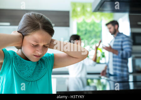 Trauriges Mädchen für ihre Ohren während die Eltern streiten im Hintergrund Stockfoto