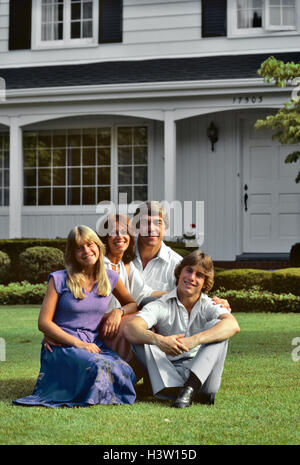 1970S 1980S FAMILIE SITZT AUF RASEN VOR S HAUS BLICK IN DIE KAMERA Stockfoto