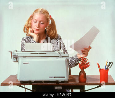 1970ER JAHRE JUNGE FRAU BLONDE HAARE AN ELEKTRISCHEN HERMES SCHREIBMASCHINE NACHDENKLICH NACHDENKLICH STUDENT TYPISIERUNG TRAGEN HAAR IN ZÖPFEN Stockfoto