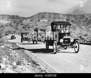 1960ER JAHRE LINIE DER 1920ER JAHRE MODELL T UND 1930ER JAHREN MODELLIEREN EINE FORD-AUTOMOBILE AUF SCHOTTERSTRAßE IM SÜDWESTEN DER USA Stockfoto