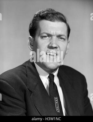 1950ER JAHRE-MANN-BETRIEB IN ANZUG UND KRAWATTE MACHEN SKEPTISCH LUSTIGES GESICHTSAUSDRUCK BLICK IN DIE KAMERA Stockfoto