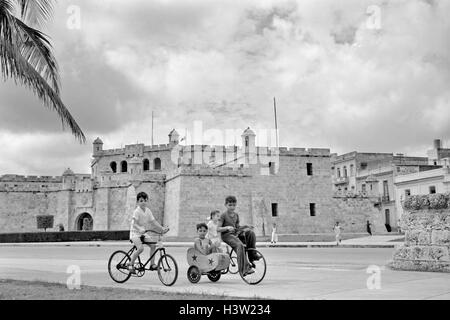 1950ER JAHREN VIER KINDER AUF FAHRRÄDERN, BLICK IN DIE KAMERA ZU AVIENDA DEL PUERTO HAVANNA KUBA Stockfoto