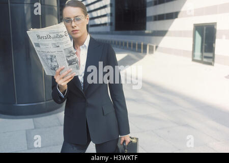 Geschäftsfrau, Aktentasche, Zeitung, lesen, halbe Porträt, Bürogebäude, Beruf, Geschäft, Frau, Anzug, Manager, Gläser, ernst, Interessen, gehen, Aktentasche, Zeitung, Werbung, anzeigen, Informationen, Nachrichten, Nachrichten, Aktualität, Geschäft prem Stockfoto