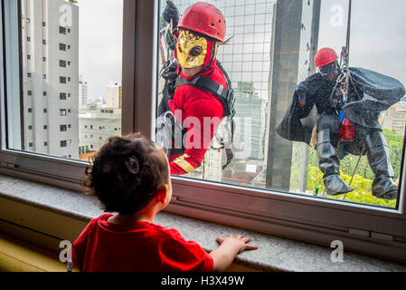 Sao Paulo, Brasilien. 11. Oktober 2016. Männer als Superhelden die Fenster putzen und mit einem Kind im Kinderspital der Sabara in der Innenstadt von Sao Paulo, Brasilien, am 11. Oktober 2016 interagieren verkleidet. Verschiedene Aktivitäten wurden in Brasilien vor die Kinder Tag in Brasilien statt, der am 12. Oktober fällt. © AE/Xinhua/Alamy Live-Nachrichten Stockfoto