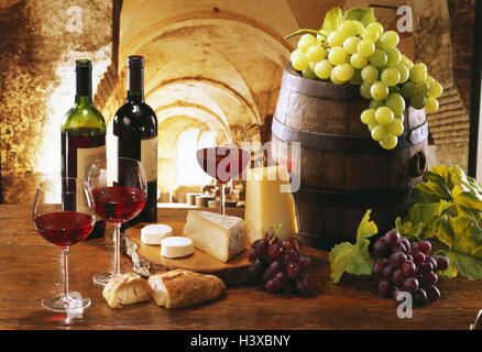 Holztisch, Weinkeller, zwei Flaschen Rotwein, drei gefüllte Gläser, hölzerne Sprungbrett mit Käse, Brot, Lauf, weißen und roten Trauben Stockfoto