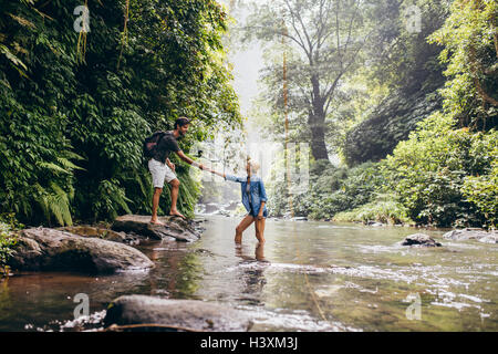 Junge Paare, die über Strom, während der Mann hilft Frau. Mann und Frau, Wandern in der Natur zu genießen. Stockfoto