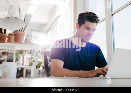 Junger Geschäftsmann mit Laptop-Computer im Büro. Junge männliche Führungskraft an Notebook an seinem Schreibtisch arbeitet. Stockfoto