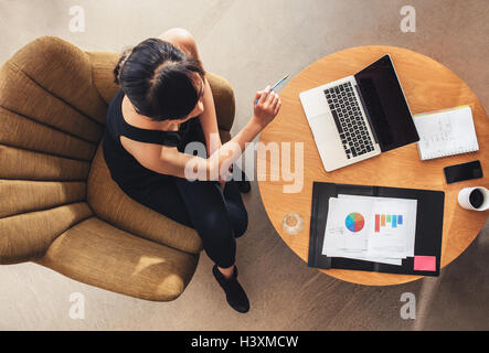 Blick von oben auf die junge Frau, die am Tisch sitzt, mit Laptop und Karten. Geschäftsfrau, die an einem neuen Geschäftsprojekt in der Bürolobby arbeitet. Stockfoto