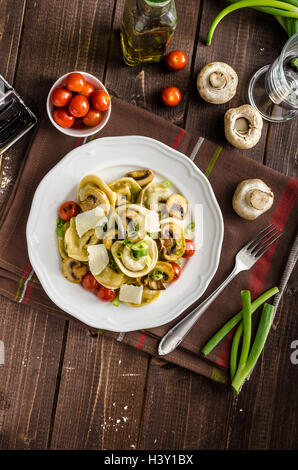 Hausgemachte Tortellini gefüllt mit Pilzen und Frühlingszwiebeln, gerösteten Tomaten, Knoblauch Souce gekrönt parmesan Stockfoto