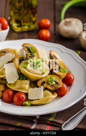 Hausgemachte Tortellini gefüllt mit Pilzen und Frühlingszwiebeln, gerösteten Tomaten, Knoblauch Souce gekrönt parmesan Stockfoto